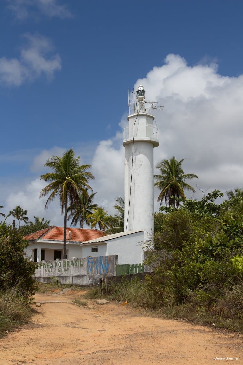 O farol, sem visitação, cercado de coqueiros. 