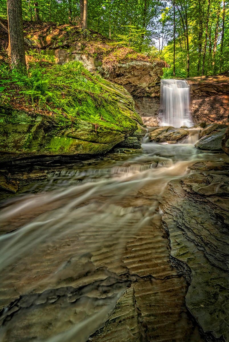 Choose your route to the beautiful 15-foot Blue Hen Falls in Ohio's Cuyahoga Valley National Park. Get to the Blue Hen Falls parking lot by 9:30 am and you might find a space. From there it's a steep half-mile hike. Parking lot full? Hike 1.5 miles from the Boston Store Visitor Center.