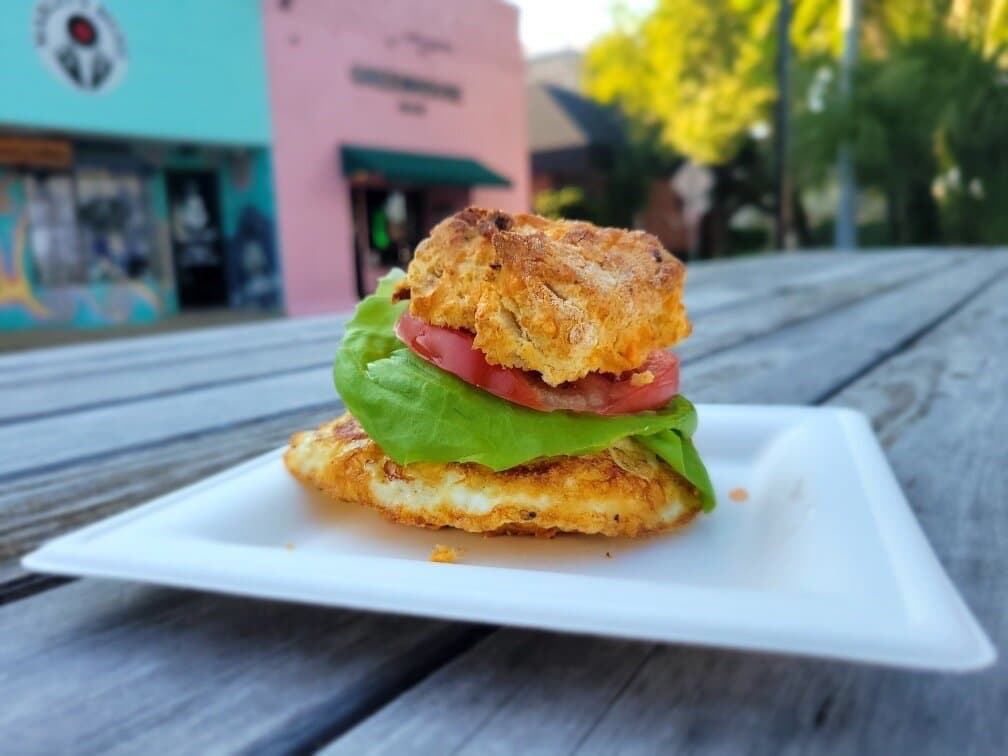 Bacon Cheddar Breakfast Sammie.  Bacon cheddar biscuit with fried farm egg*, tomato, lettuce, brown mustard