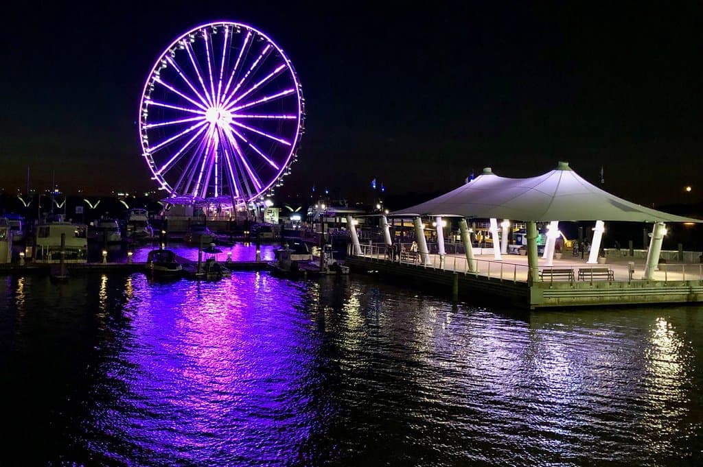 Ferris Wheel at night showing off its neon lights in the water on the National Harbor.
