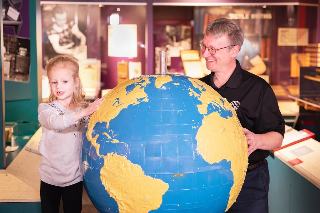 Museum Director, Micheal Hudson, interacts with visitor around a tactile globe.