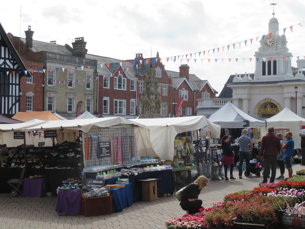 Market in Market Place from a lunch bench outside Costa Coffee - historic fountain at centre and potting plants, shoes and reconditioned Dyson vacuum cleaners for sale out front.