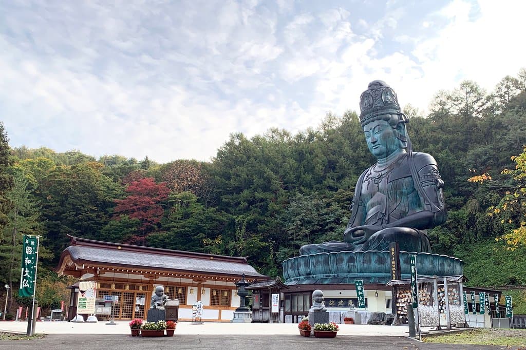 　青森市郊外、桑原の地に横たわる稲山は、春には山桜と新緑がみごとな彩りをなし秋には錦を織りなす。まるで天然の屏風のよう。その稲山の眼下には日本の原風景を思わせる田園風景が広がっています。
　日本最大の青銅坐像仏、昭和大仏はこの豊かな自然に囲まれた稲山の中腹に鎮座しています。境内地には東日本最大の木造五重塔が屹立し、金堂、開山堂、大師堂、書院が甍を並べ、広大な枯山水庭園「忘帰庭」が訪れる人に落ち着きを与えてくれます。青龍寺伽藍の多くは天然青森ひばを資材に用い、青森の名工、大室勝四郎棟梁が持てる技量を尽くしました。
　「伽藍が無言の説法をする」開基織田隆弘師の熱い信念がこの霊場を開き、今もなお全山を満たしています。
　日々の喧噪を離れた心静かな時を求めて、国内はもとより世界各国から参拝者が訪れています。