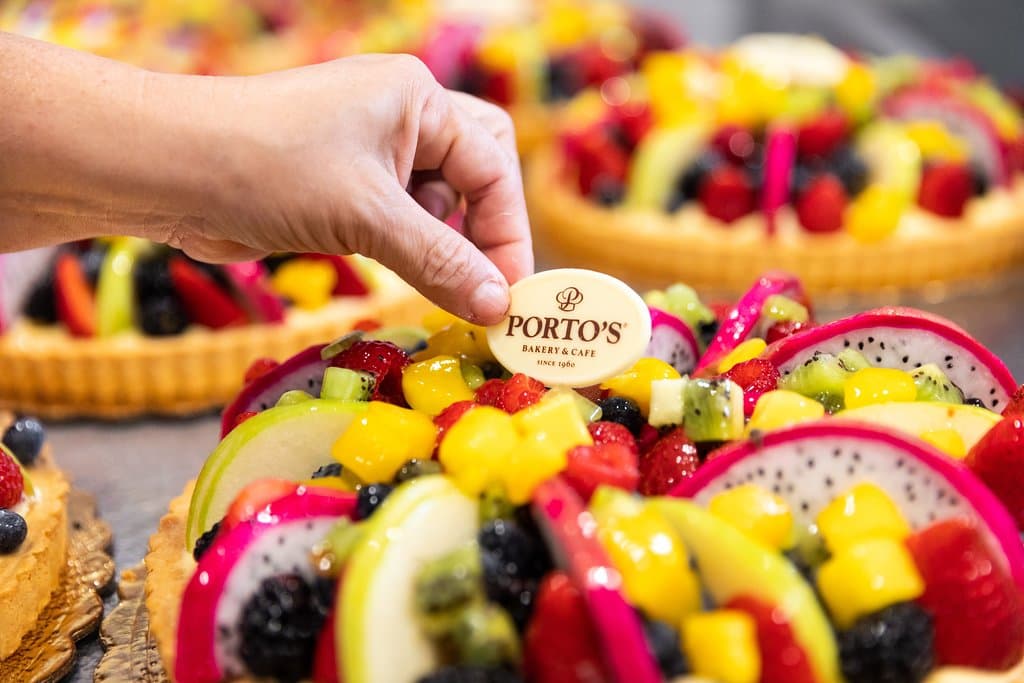 Fresh Fruit Tart
A sweet, buttery short dough shell (Pâte Sucrée) filled with our homemade vanilla custard and a thin layer of yellow sponge cake, topped with an assortment of fresh fruit, a thin layer of apricot glaze and a white chocolate Porto’s plaque