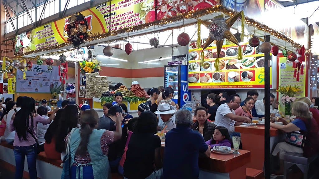 Several eating counters in the market, all full of patrons.