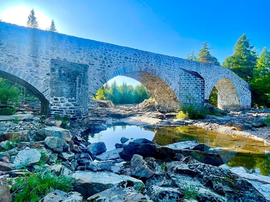 This handsome & robust old bridge dates back to around 1752 - another one of Major William Caulfield’s bridges , erected during his expansion of military roads across Scotland . It has masonry arches crossing the river Dee, and the views are of natural unspoiled highland countryside.