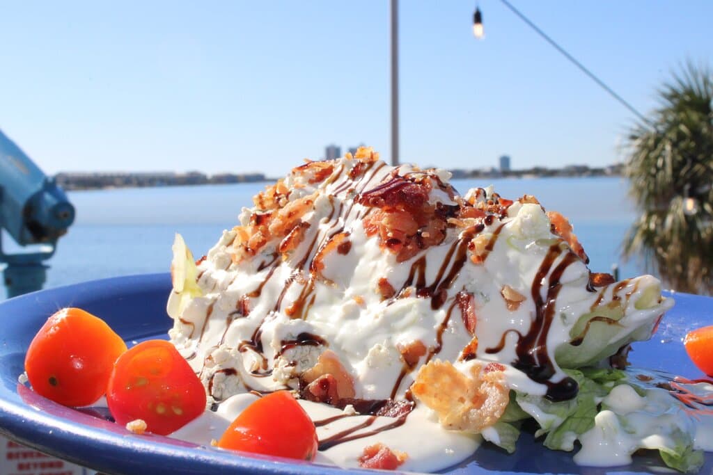 Wedge Salad - a quarter head of iceberg lettuce with blue cheese crumbles, applewood bacon, cherry tomatoes, blue cheese dressing and a balsamic glaze drizzle
