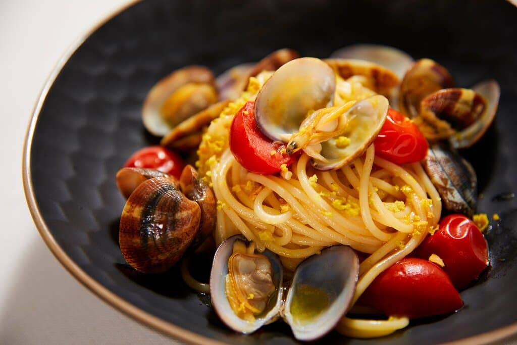 Un classico rivisitato con cura e attenzione al dettaglio. Gli spaghetti aglio, olio e vongole sono realizzati con gli spaghetti del prestigioso pastificio Mancini, hanno una consistenza perfetta che cattura il sapore delle vongole fresche. Il piatto è arricchito da qualche pomodorino, che aggiunge una nota di dolcezza, e completato con un crumble di grano croccante, che dona un piacevole contrasto di consistenze.