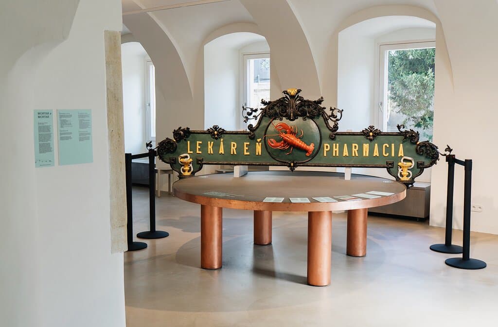 The renovated premises of the Red Crayfish Pharmacy combine the atmosphere of a preserved baroque pharmacy with modern visitor services. Part of the building still consists of a rebuilt medieval barbican—an important defensive element of the city walls.  For many years, the pharmacy housed an exhibition of pharmacy history. Today, the space provides visitor services for St. Michael’s Tower, and an exhibition space dedicated to the theme of medieval defense in Bratislava.