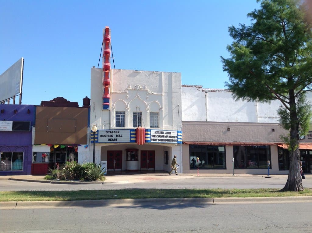 The facade of the Texas theatre. The body of the theatre is the white building in the background